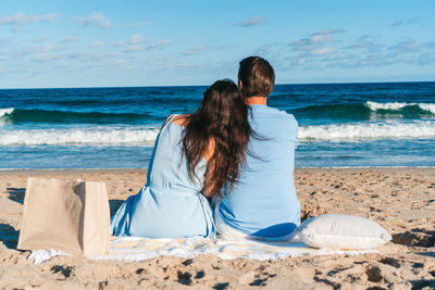 Rear view of woman sitting at beach against sky