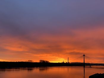 Silhouette bridge over bay against sky during sunset