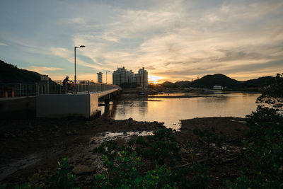 River by city buildings against sky during sunset