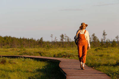 Naturalist woman exploring wildlife and ecotourism adventure walking on path through peat bog swamp.