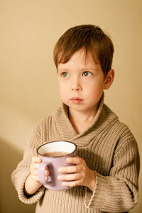 Boy drinks cocoa. warm autumn photography. a boy in a brown sweater drinks from a mug.