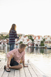 Young man looking away while woman fishing on pier at lake