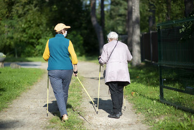 Rear view of two senior women with face masks  nordic walking poles during covid-19 pandemic