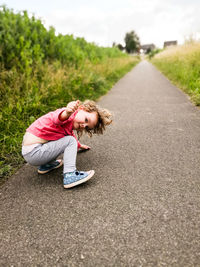 Portrait of cute girl crouching on footpath amidst plants