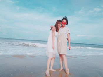 Full length of smiling friends standing at beach against sky