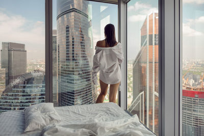 Woman in white shirt stand on the bed window in a skyscraper near the bed