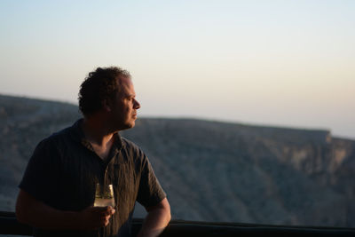 Young man looking at mountains against sky with a drink