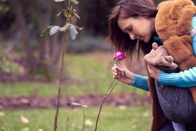 Woman holding flower while standing outdoors