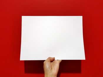 Low section of person holding paper against red background