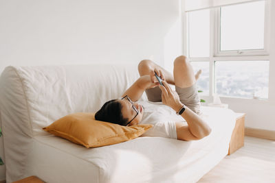Full length of man using mobile phone while lying on sofa at home