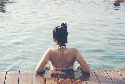 Rear view of shirtless man sitting on pier over sea