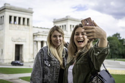 Happy woman taking selfie with friend against built structure