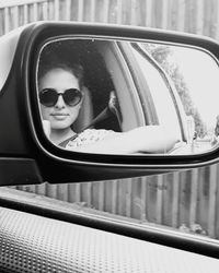 Portrait of young woman wearing sunglasses reflecting on car side-view mirror