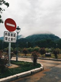 Road sign by trees against sky