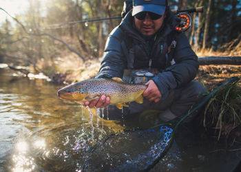 A man catches a large brown trout on a river in maine