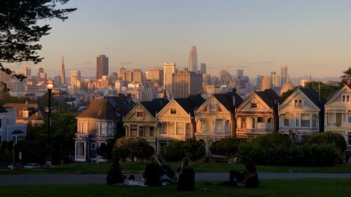 Group of people in front of buildings against sky during sunset