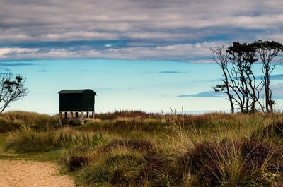 Scenic view of hut at seaside against cloudy sky 