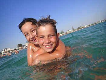 Portrait of smiling siblings swimming in sea against sky