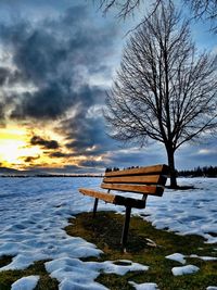 Empty bench against cloudy sky