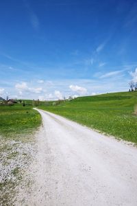 Empty road amidst field against sky