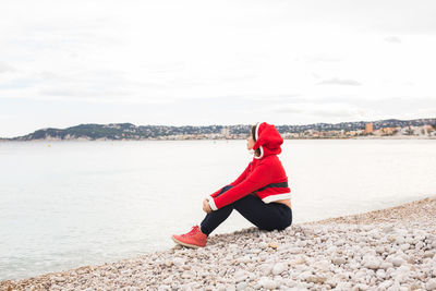 Woman sitting on pebbles at beach against sky