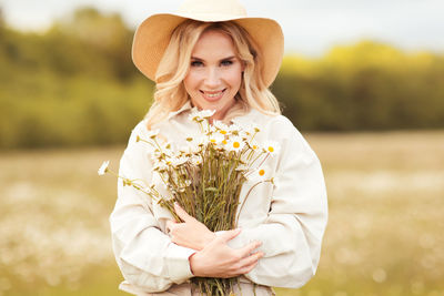 Portrait of smiling woman holding flowers on field