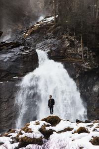 Male hiker standing on hill near waterfall in highland area in winter