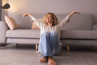 Cheerful woman sitting by sofa at home