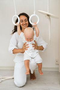 Baby is hanging on child indoor gym playset on wooden gymnastics rings. kid swinging in playroom