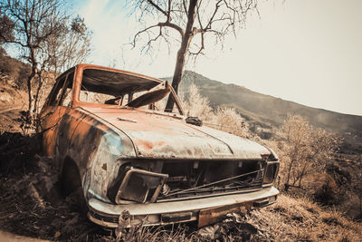 Abandoned car on field against sky