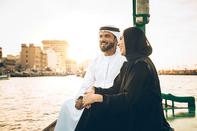 Cheerful couple talking while sitting in boat on river in city