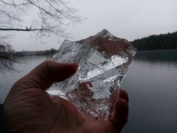 Close-up of hand on frozen lake against sky