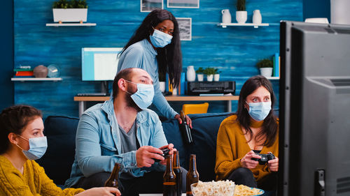 Cheerful people wearing mask while playing video game at home