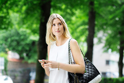 Young woman holding mobile phone while looking away outdoors