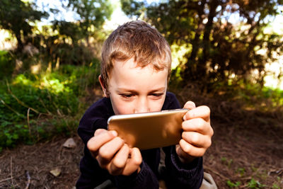 Boy holding mobile phone while sitting outdoors