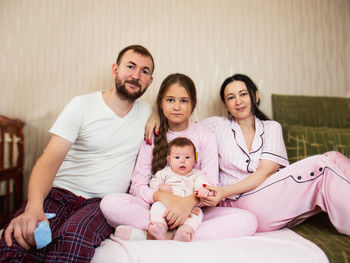 Portrait of a family of four, dad, mom, eldest daughter and baby daughter are sitting on the sofa