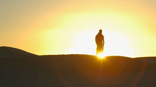 Silhouette man standing against bright sun during sunset