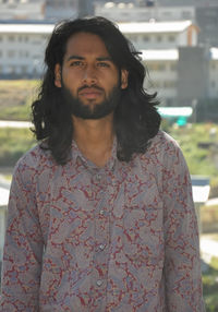 A long haired and bearded good looking young man looking straight while standing outdoor