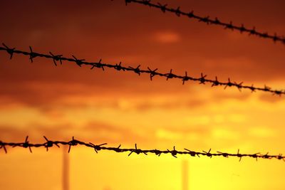 Close-up of barbed wire fence against sky during sunset