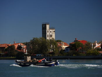 Boats in river by buildings in city against clear blue sky