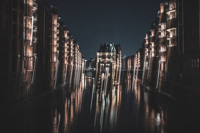 Illuminated buildings by river against sky at night