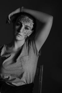 Portrait of beautiful young woman with paper on face against black background