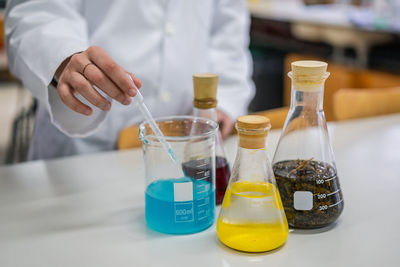 Unrecognizable chemist taking blue fluid with pipette while conducting experiment in modern lab