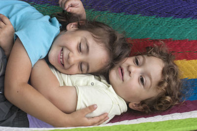 High angle view of loving siblings lying on textile