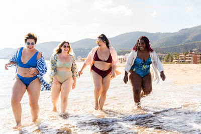 Side view of smiling friends standing at beach