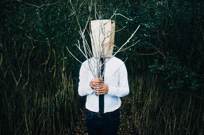 Man in forest holding branches with paper covering face