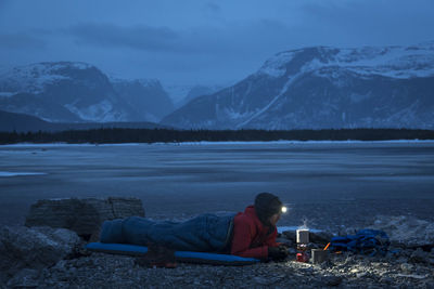 Man relaxing on snowcapped mountains by lake against sky