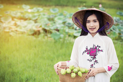 Portrait of smiling young woman with buds in basket standing on field