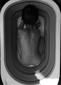 Rear view of shirtless boy in bathroom tub