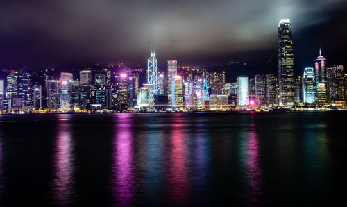 Illuminated buildings by river against sky at night
